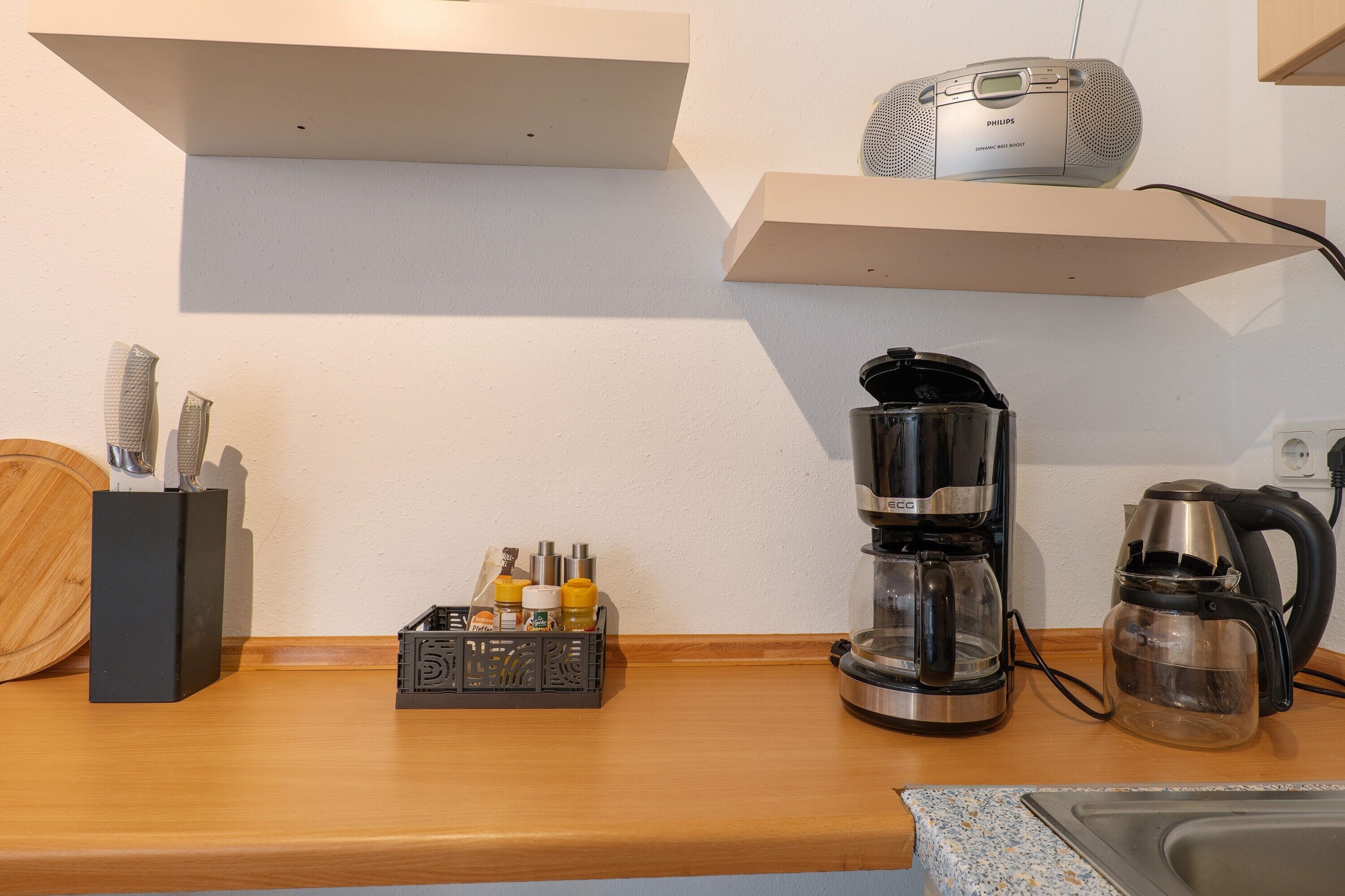 Una cocina con cafetera, hervidor y un radio Philips sobre una estantería.