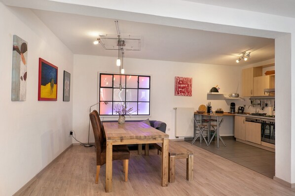 A modern kitchen with a dining area, wooden flooring, and artwork on the walls.