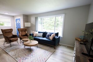 A living room with a blue sofa, two brown armchairs, a coffee table, and a large window. - Centrally located, newly renovated home (Federal Way)