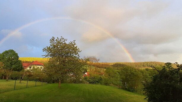 A rural landscape with a house, a tree, and a rainbow.