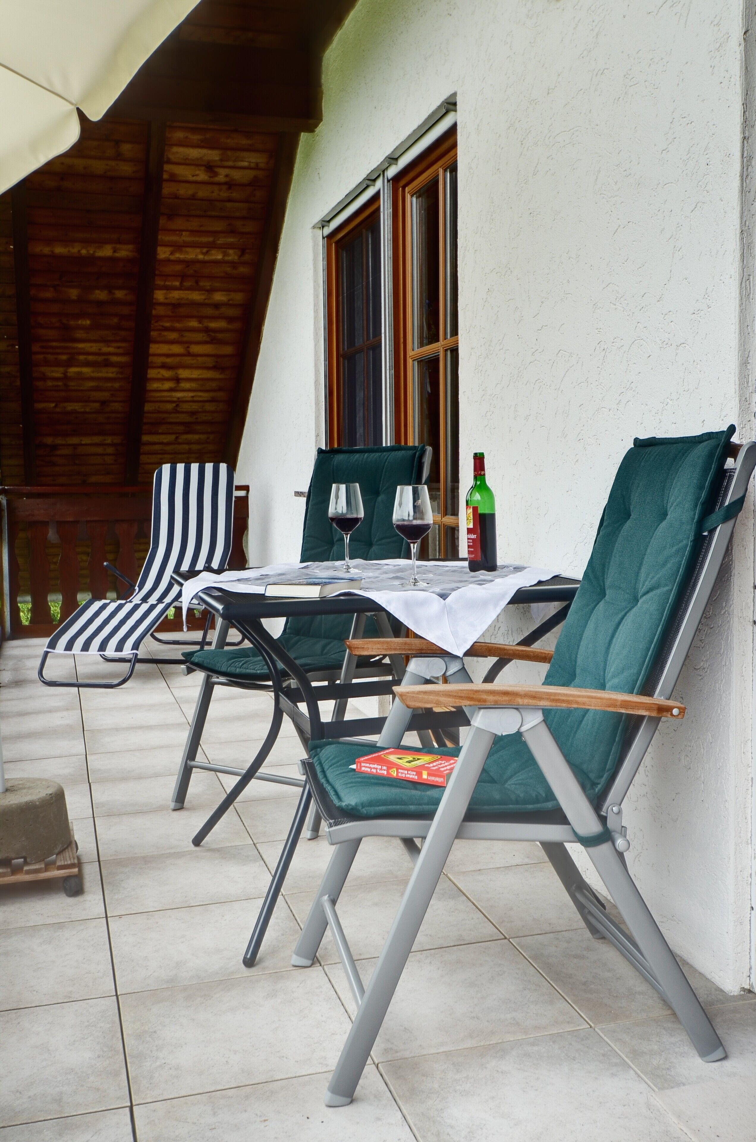 A patio with two chairs, a table, and a bottle of wine.