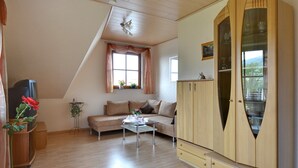 A room with a sofa, a glass coffee table, a wooden cabinet, and a television.