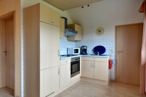 Una cocina con armarios de tonos claros, un microondas, una estufa y un reloj en la pared.