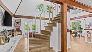 A spacious living area with a wooden staircase, a fireplace, and a dining area with a view of the outdoors. - Private Lake House near Enterprise (New Brockton)