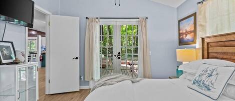 Ein Schlafzimmer mit einem Bett, einem Fernseher, einem Schrank, einem Fenster mit Vorhängen und einem Bild an der Wand.
