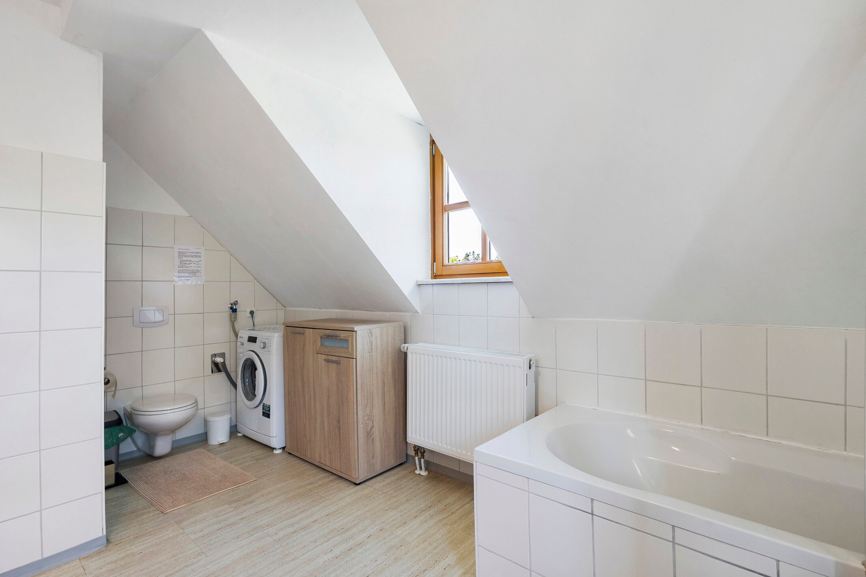 A small, clean bathroom with a washing machine, a toilet, and a bathtub.