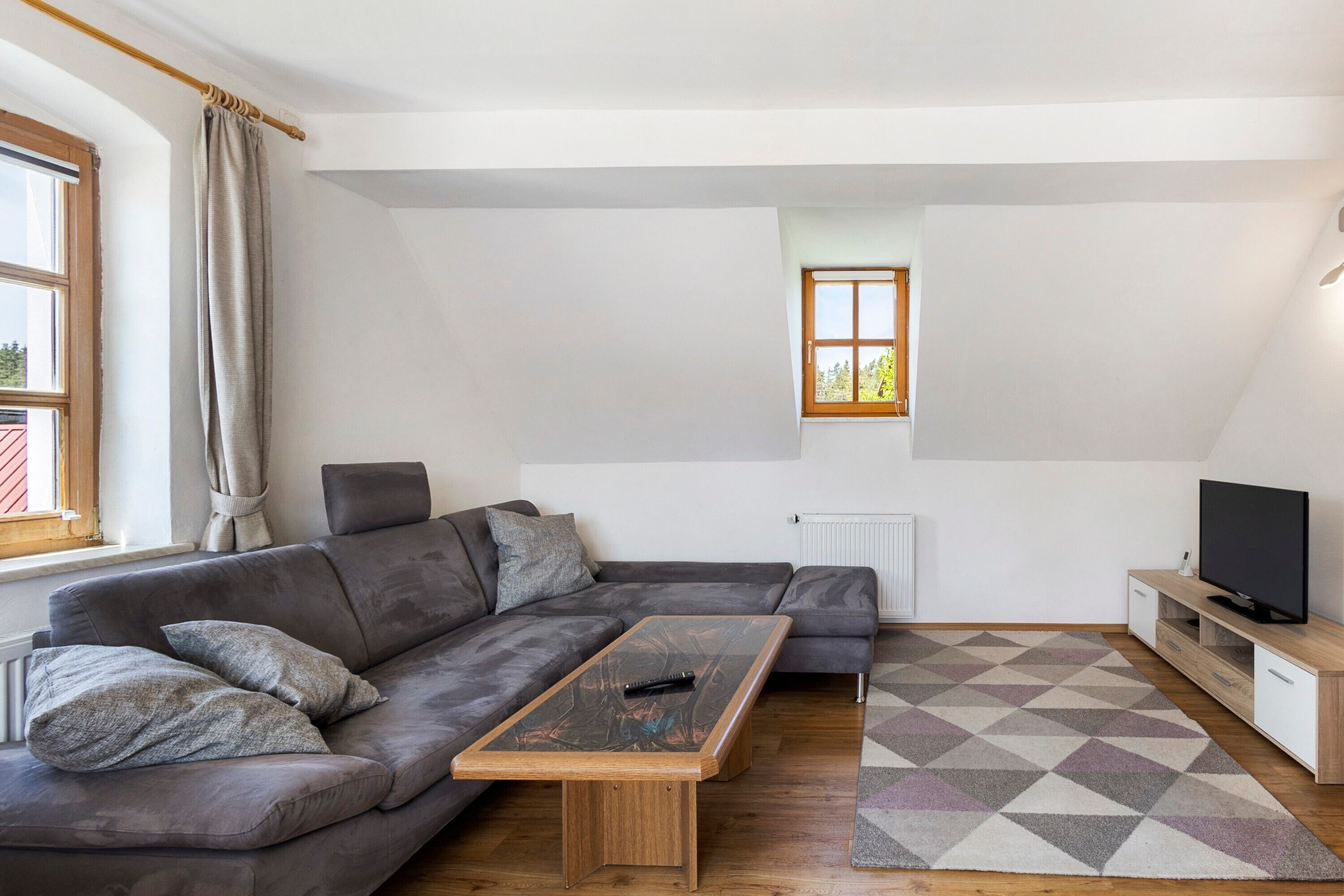 Una sala de estar moderna con un sofá modular, una mesa de centro, un mueble para televisión y una alfombra estampada.