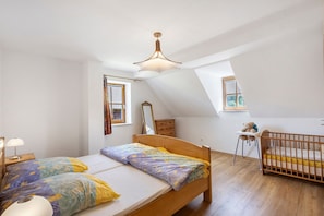 A bedroom with a sloped ceiling, a bed, a crib, a desk, and a window.
