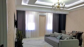 Ein modernes Wohnzimmer mit grauem Sofa, einer großen Topfpflanze und einem Chandelier.