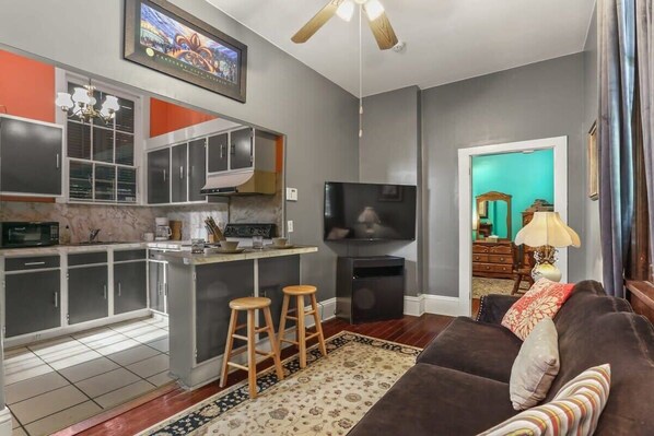 A modern living space with a kitchen, a TV, a sofa, and a ceiling fan.