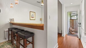 Una cocina con encimera de madera, tres taburetes de bar, lámparas colgantes y un cuadro en la pared.