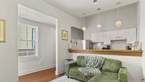 Una sala de estar con un sofá a rayas verdes, un tapete estampado y una cocina con armarios blancos y encimera de madera.