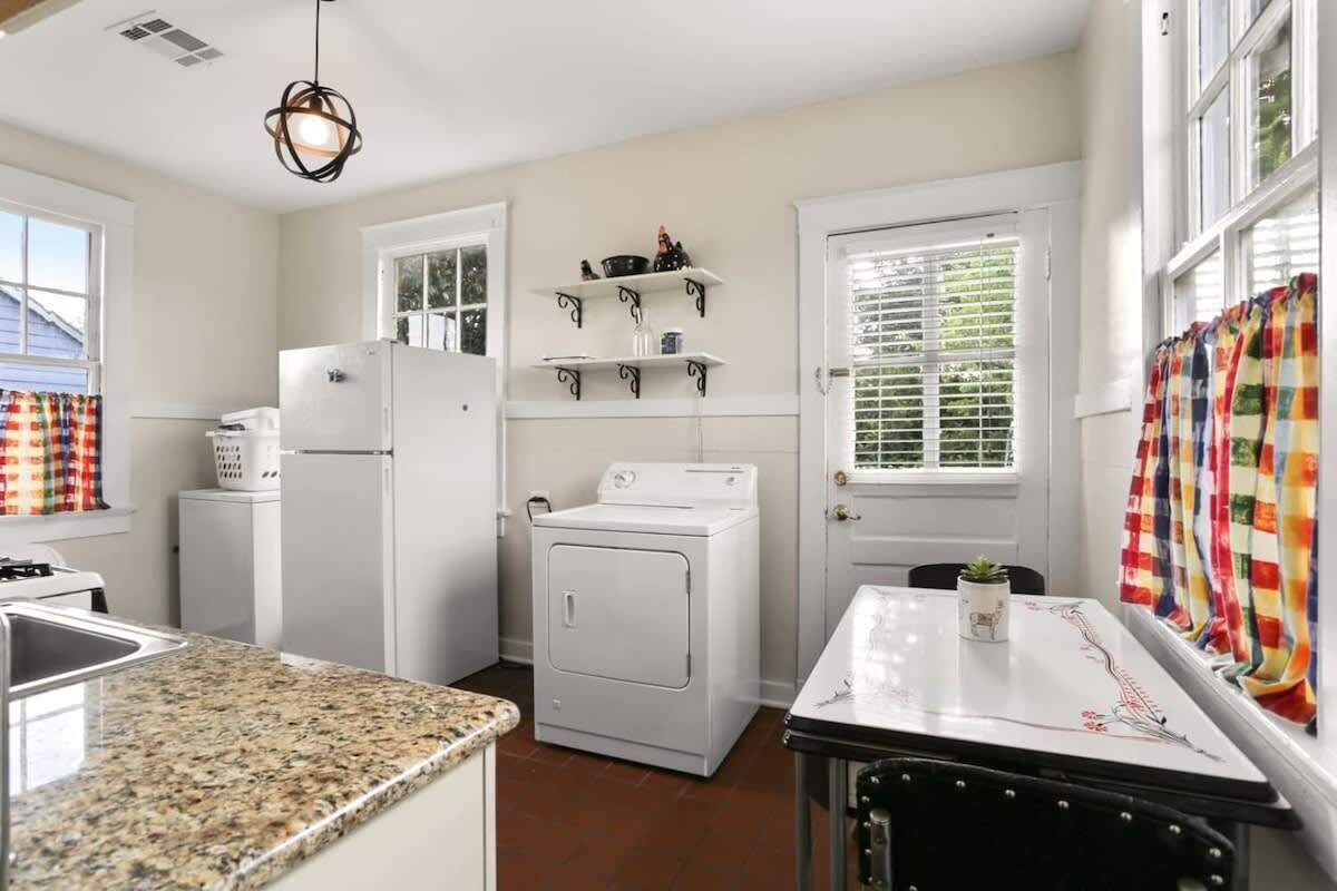 A kitchen with a granite countertop, a refrigerator, a washing machine, and a dining table with a plant.