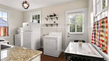 A kitchen with a granite countertop, a refrigerator, a washing machine, and a dining table with a plant.