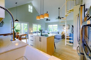 A spacious kitchen with a central island, a dining area with a table and chairs, a living room with a sofa and a TV, and a staircase leading to an upper level. - Boater's Paradise | 170' Waterfront | 30' Dockage | Ramrod Key Retreat (Ramrod Key)
