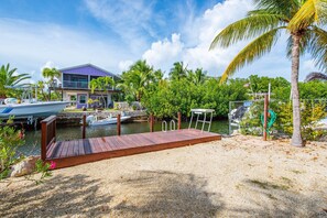 Un muelle con plataforma de madera, una casa de techo morado y una palmera.