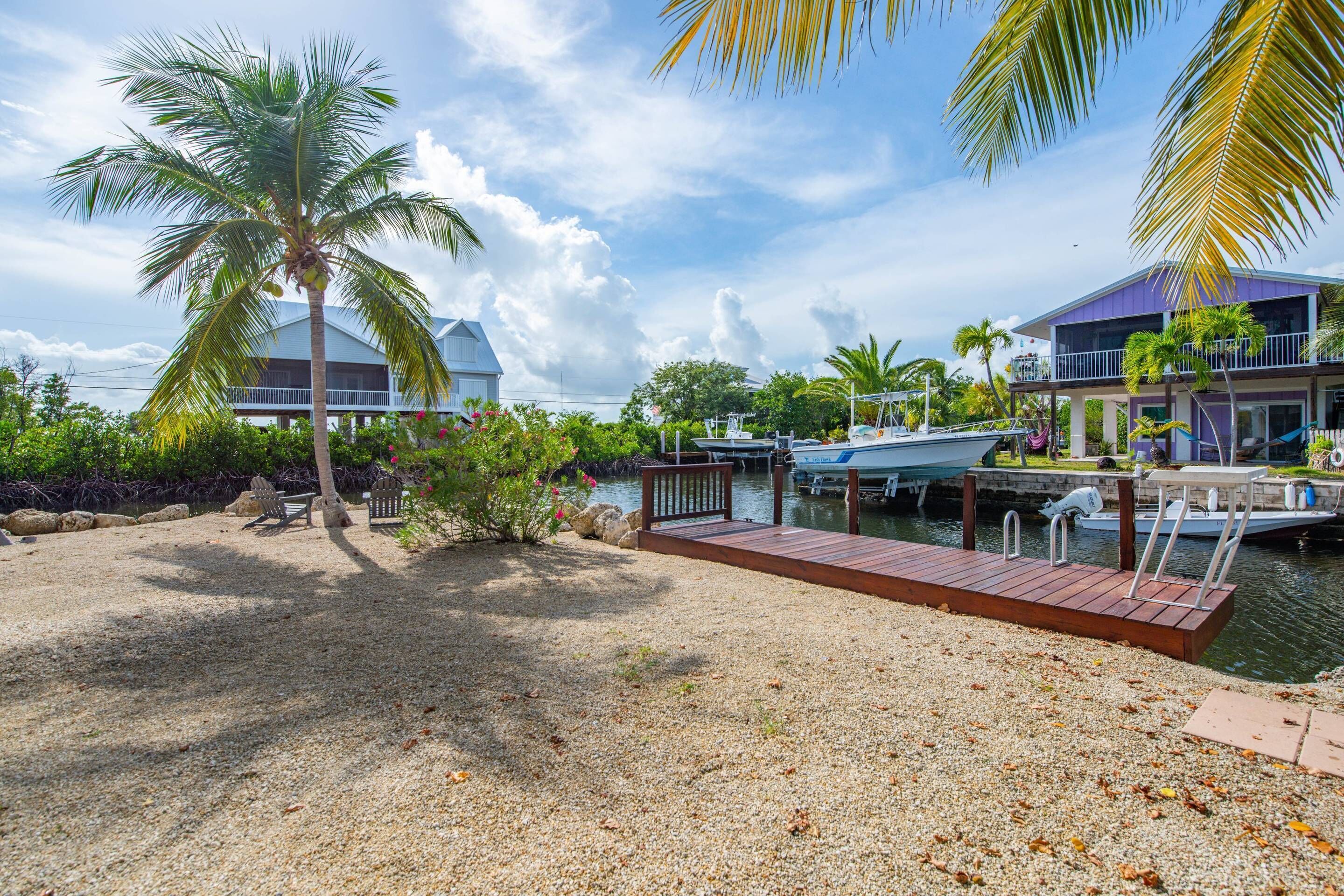 A waterfront property with a dock, palm trees, and a house with a balcony overlooking the water.