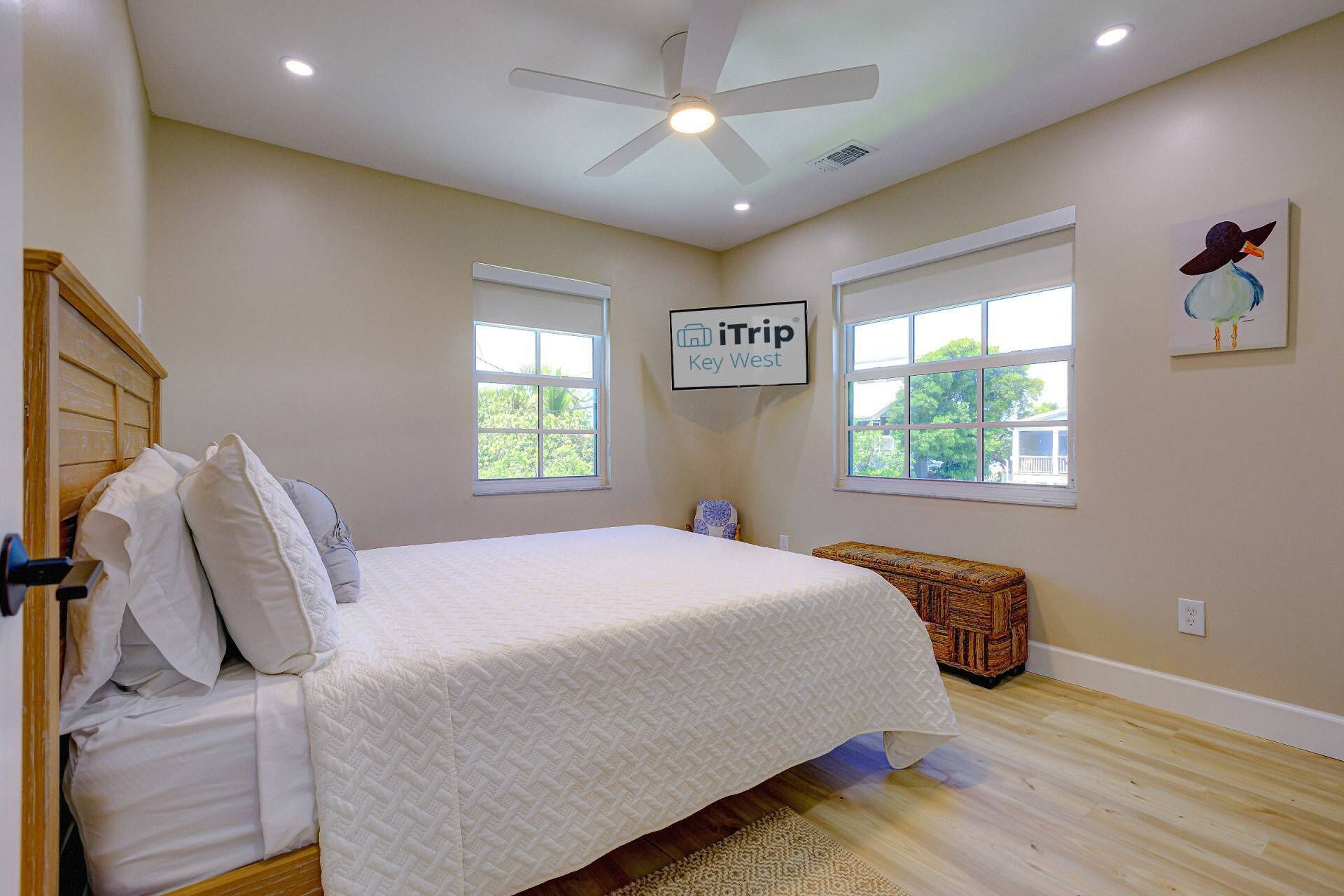 A bedroom with a bed, two windows, a ceiling fan, and a sign on the wall.