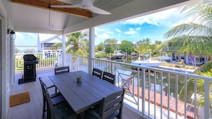 A covered outdoor area with a table and chairs, a ceiling fan, and a view of a marina with boats and palm trees. - Boater's Paradise | 170' Waterfront | 30' Dockage | Ramrod Key Retreat (Ramrod Key)