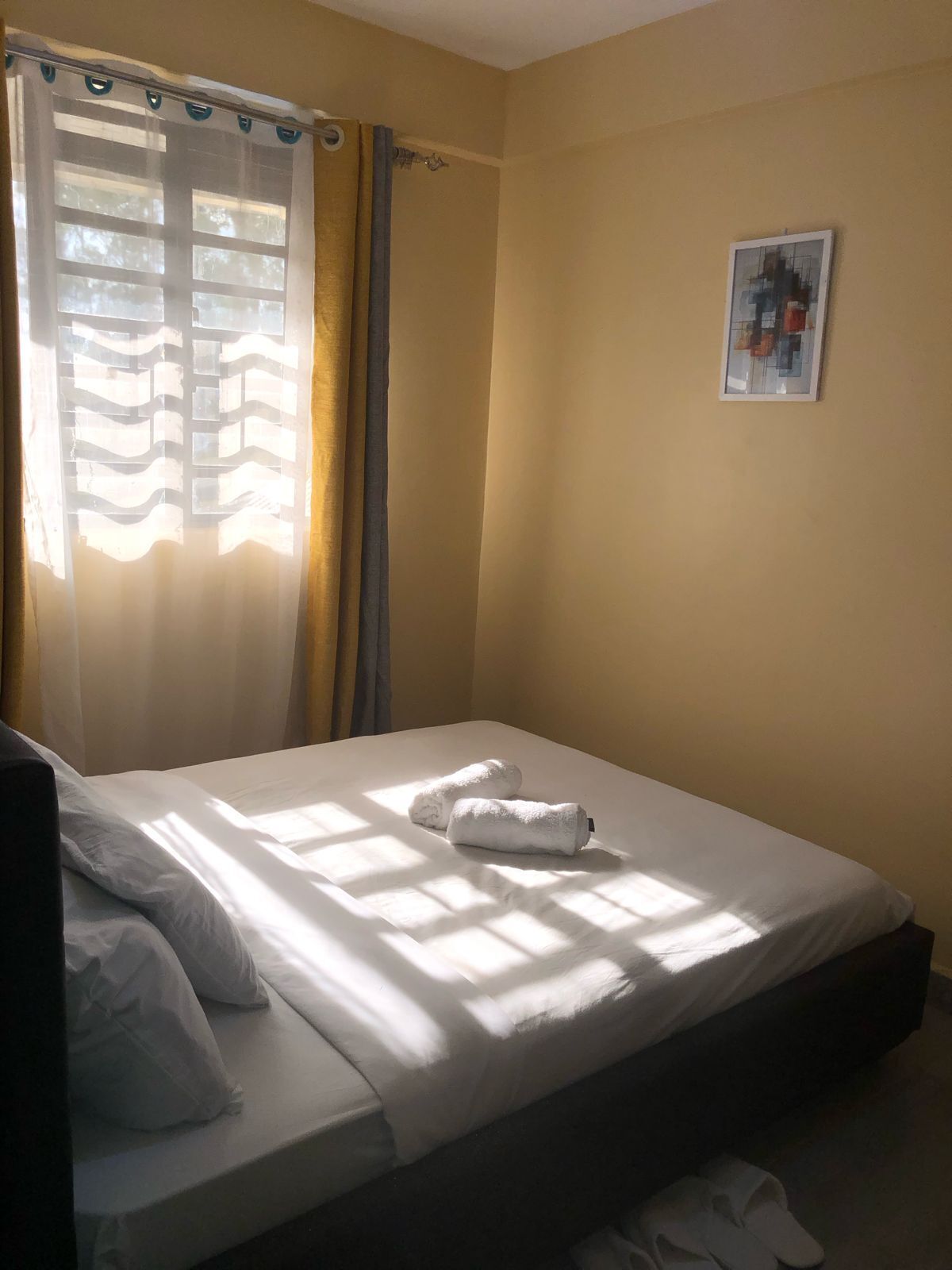 A single bed with white linens, a pair of towels, and a pair of slippers on the floor.
