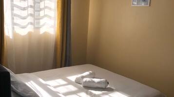 A single bed with white linens, a pair of towels, and a pair of slippers on the floor.