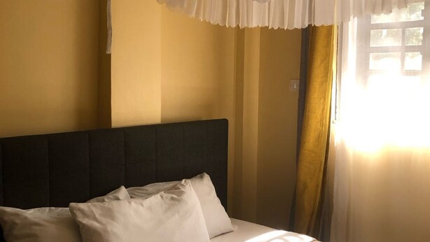 A bed with white linens, a dark headboard, and a white canopy.