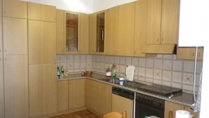 Una cocina con armarios de madera, encimera de granito, lavavajillas y una silla.