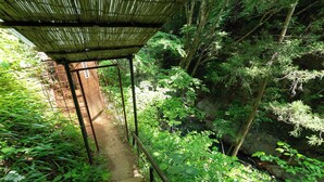 A staircase leading into a forested area with a bamboo structure overhead. - Tabist Shiobaraonsen Kashiwaya Ryokan (Nasushiobara)