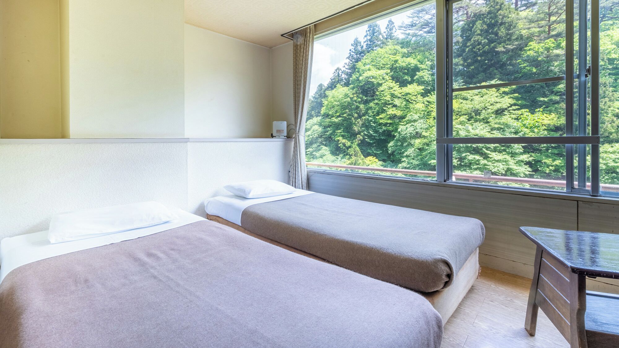 Een kamer met twee bedden, een klein tafeltje en een raam met uitzicht op een bos.