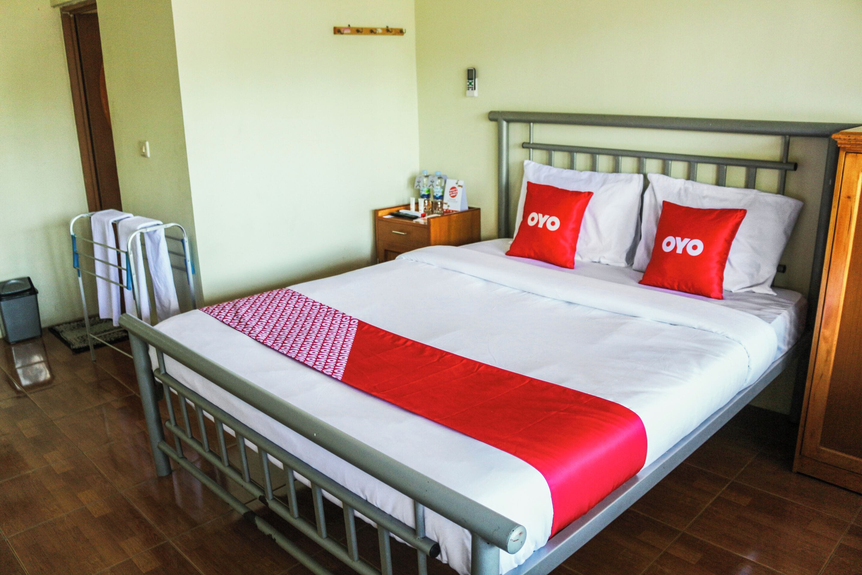 A neatly made bed with a metal frame, a wooden nightstand beside it, and a towel rack against the wall.