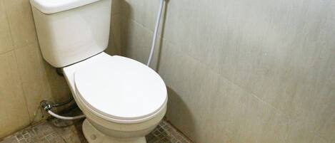 A standard white toilet with a tank and a bidet attachment in a bathroom with tiled flooring.