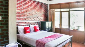 Ein Einzelbett mit einer rot-weiß gemusterten Tagesdecke, eine Ziegelwand, ein Fernseher auf einem Schrank und ein Fenster mit Blick nach draußen.