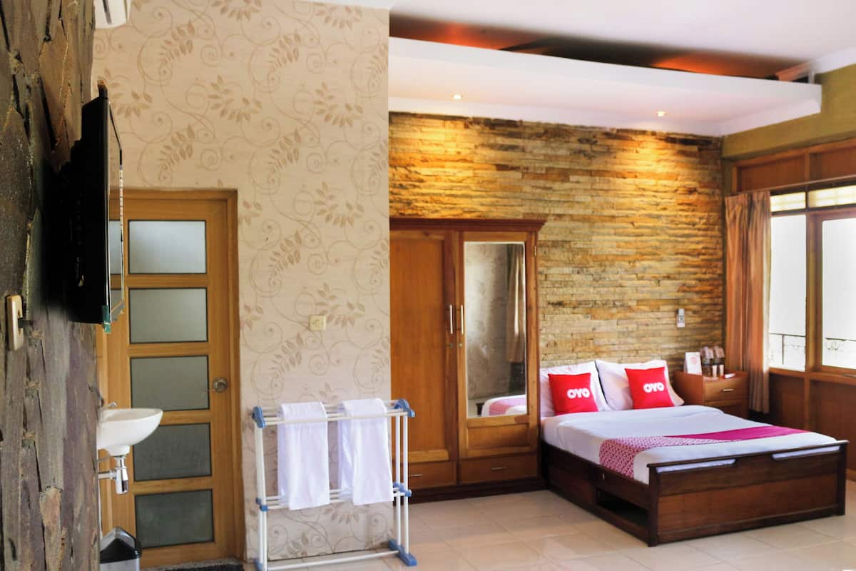 A bedroom with a wooden bed, a wardrobe, a mirror, and a bathroom with a sink and towel rack.