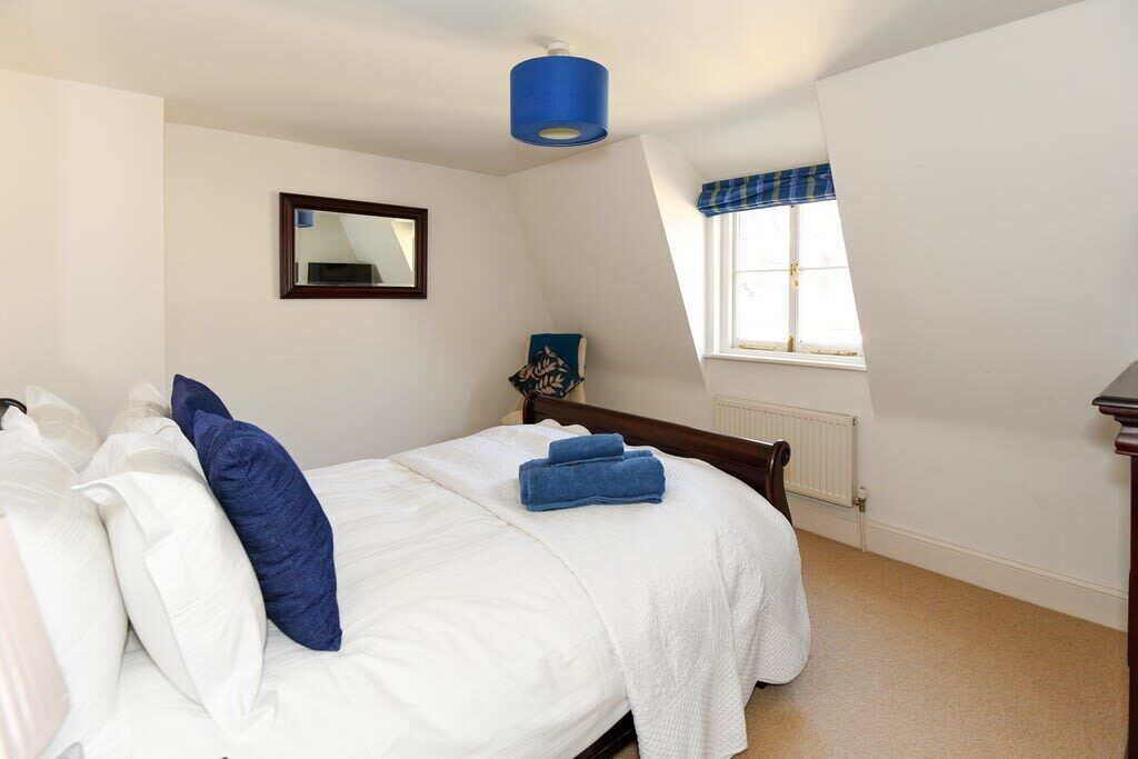 A bedroom with a bed, a bedside table, a lamp, a window with a view, and a mirror on the wall.