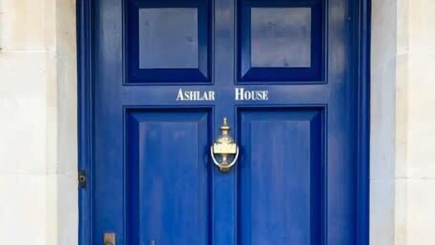 Een blauwe deur met de naam "ASHLAR HOUSE" en een messing klink.