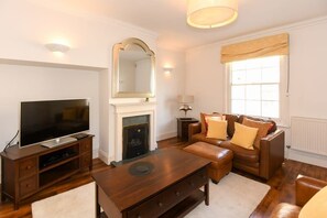 A living room with a flat-screen TV, a fireplace, leather sofas, and a wooden coffee table. - Spacious Townhouse, Private Parking, Central Wells (Somerset)