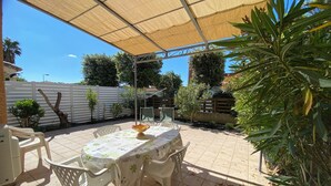 Un patio couvert avec une table et des chaises, entouré de plantes et d’une clôture blanche.