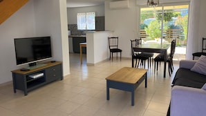 Un salon moderne comprenant un téléviseur, une table basse en bois, un canapé et un coin repas avec des chaises et une table en verre.