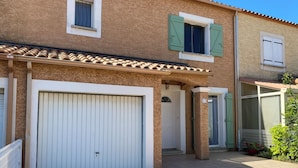 Une maison à deux étages avec une porte de garage blanche, un petit porche doté d’un toit en tuiles et une porte verte.