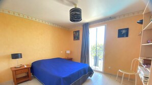 Une chambre à coucher comprenant un lit, une table de chevet, un bureau, une chaise, une fenêtre et un ventilateur de plafond.