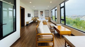 Habitación de hotel moderna con un largo banco de madera, una mesa de madera y un ventanal con vistas a la ciudad.
