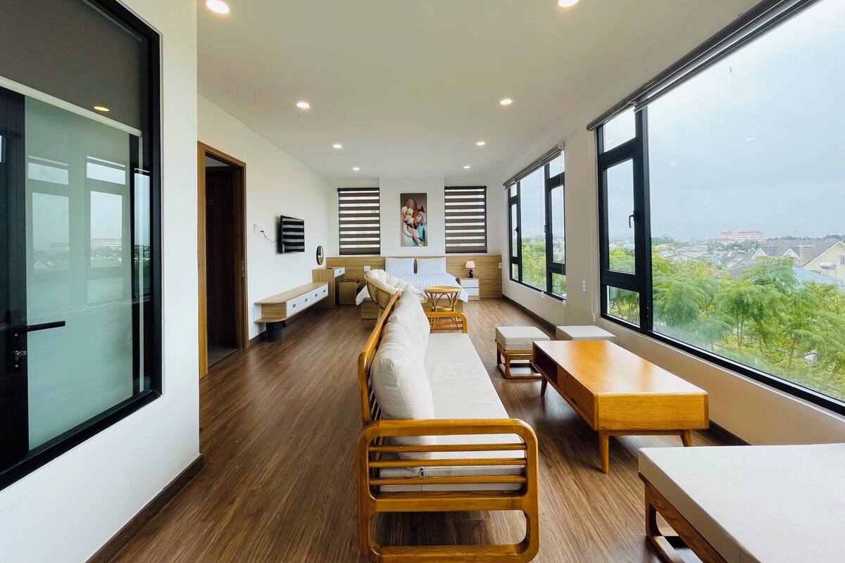 A modern hotel room with a long wooden bench, a wooden table, and a large window offering a city view.