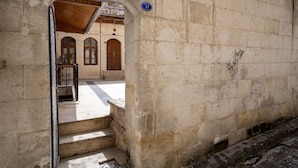 A stone building with a wooden staircase leading to an entrance, a blue sign with the number 11, and a tiled floor. - Aysel Hanım Konağı (Gaziantep)