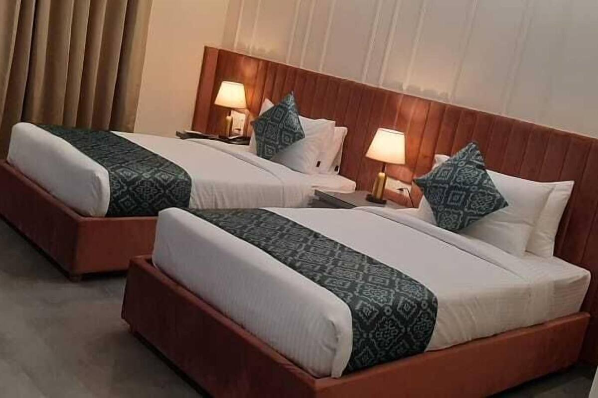 Dos camas juntas con cabeceros de madera, ropa de cama blanca y almohadones estampados.