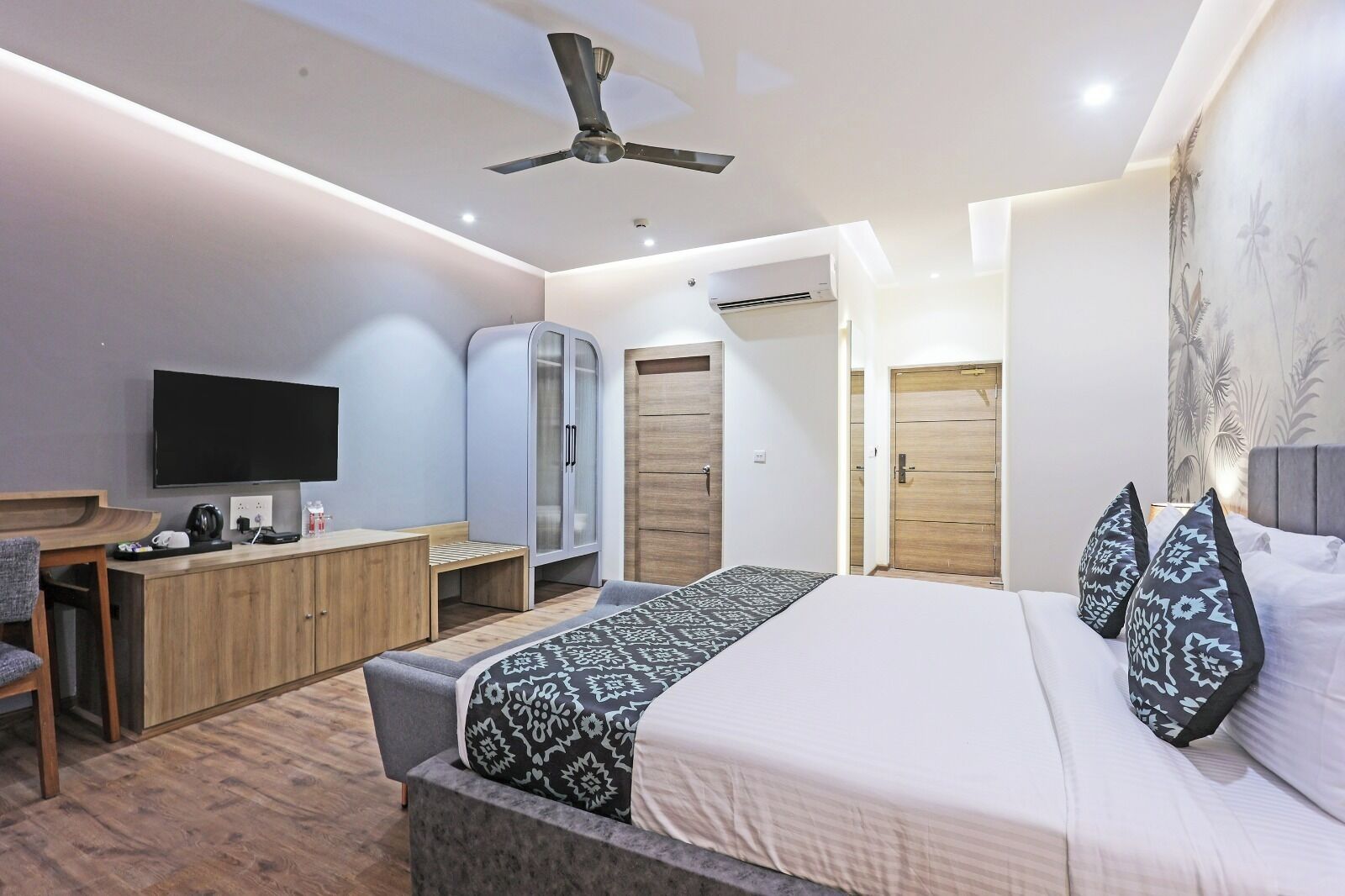 A modern hotel room with a bed, a desk, a wardrobe, and a television.