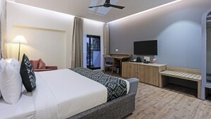 A modern hotel room with a bed, a desk, a chair, a television, and a ceiling fan. - Cocasa Boutique Hotel (Varanasi)