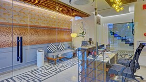 A modern office space with a glass partition, a sofa with striped cushions, a desk with a computer, and a chair. - Cocasa Boutique Hotel (Varanasi)