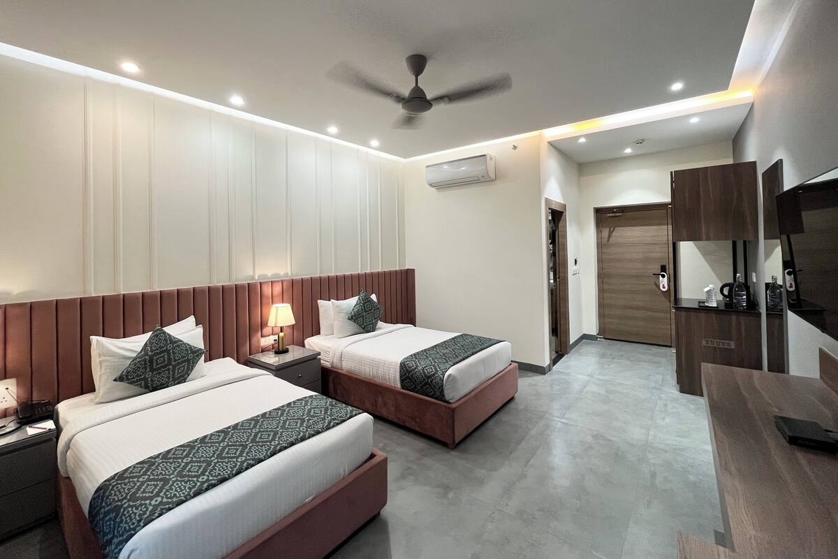 Habitación de hotel con dos camas, ventilador de techo, iluminación empotrada, televisor y minibar.
