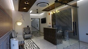 A modern interior with a geometric patterned floor, a striped sofa, a glass partition, and a staircase in the background. - Cocasa Boutique Hotel (Varanasi)