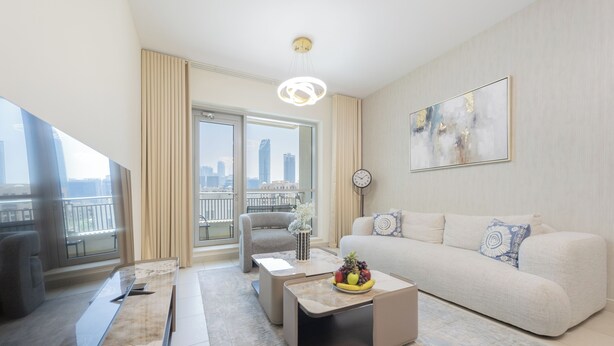 A modern living room with a sofa, coffee table, and TV. There is a balcony with a view of the city.